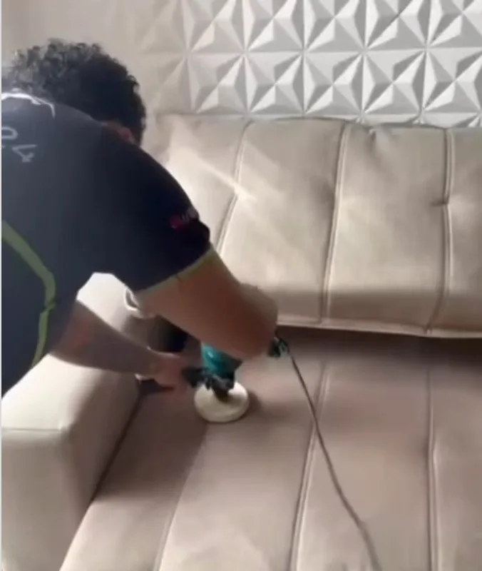Funcionário uniformizado passando a máquina de limpeza a seco em um sofá claro